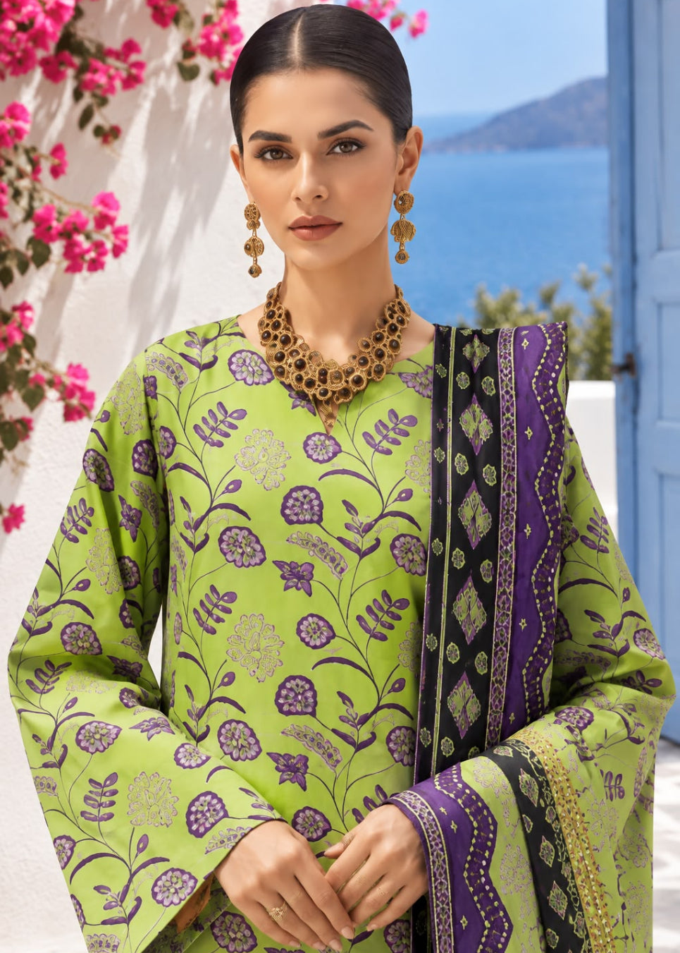 A woman models a vibrant lime green and purple printed ethnic salwar kameez set with a matching dupatta, set against a scenic background of blue sea and pink flowers.
