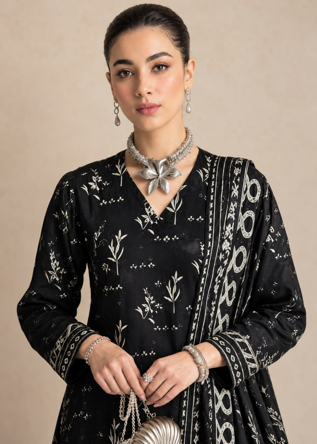 A woman modeling a black traditional outfit with white floral and geometric patterns, accessorized with silver jewelry against a neutral beige background.