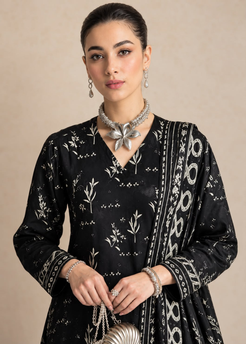 A woman modeling a black traditional outfit with white floral and geometric patterns, accessorized with silver jewelry against a neutral beige background.