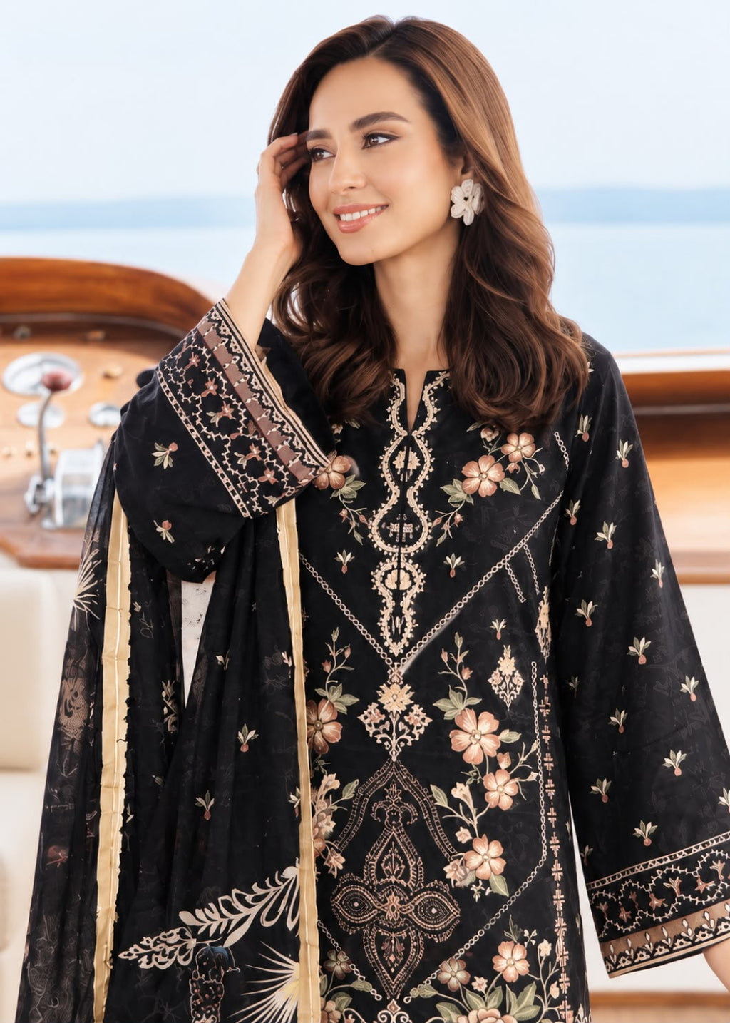 A woman wearing a black embroidered traditional outfit with floral patterns and a matching dupatta, posed on a boat with water and wooden railing visible in the background.