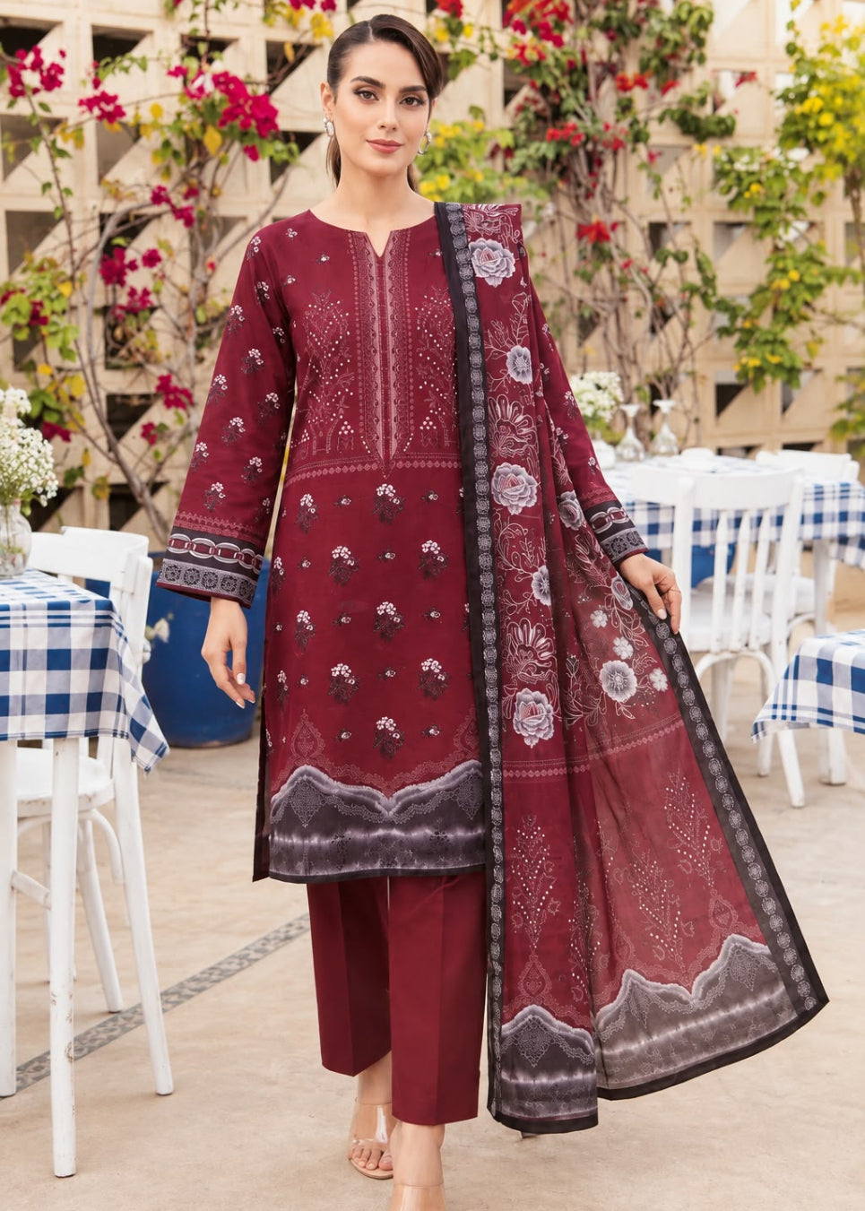 A woman models a three-piece traditional South Asian salwar kameez set in maroon. The set includes a long-sleeved embroidered kameez top, matching trousers, and a sheer dupatta with floral prints and borders.