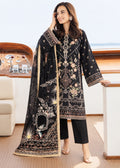 A woman models a black three-piece traditional outfit with intricate gold and beige embroidery, featuring a long kurta, black pants, and a matching dupatta, set against a luxurious yacht cabin background.