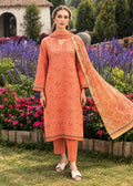 A woman stands in a garden wearing a peach-orange embroidered kurta set with matching pants and dupatta. The outfit features delicate floral embroidery and geometric border patterns, paired with white slide sandals.