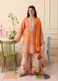 A woman modeling a traditional three-piece salwar kameez suit in a pastel-colored room. The set features an orange kurta with white embroidery, matching wide-leg trousers with a tulip print, and a coordinating orange dupatta.