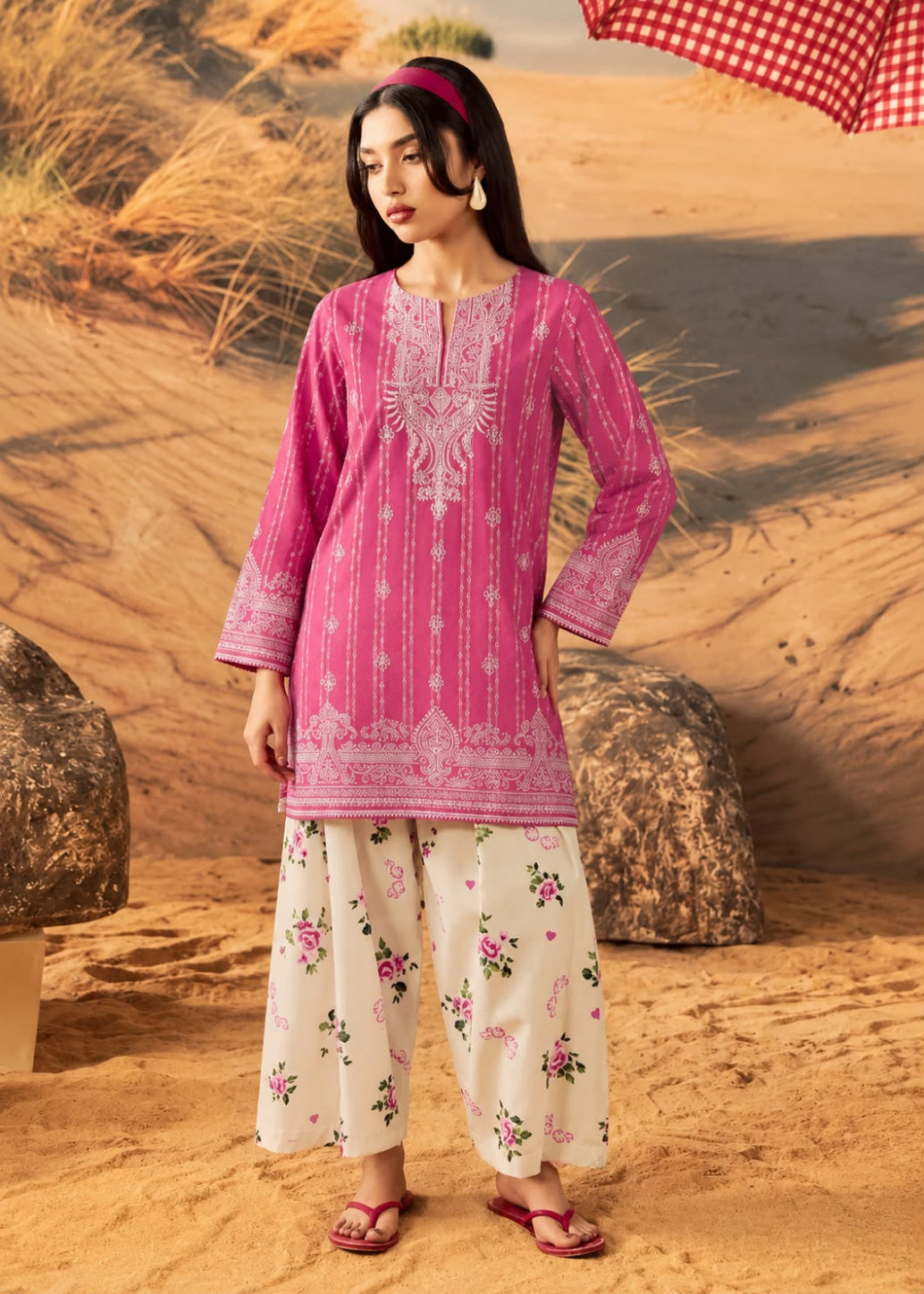 A woman modeling a pink embroidered kurta with white floral pants in a desert setting.