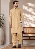 A man modeling a beige kurta and pant set in a styled indoor setting with a bench, potted plant, and natural light shadows.