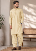 A man modeling a light beige kurta and pant set in a styled indoor setting with a bench, potted plant, and textured rug.