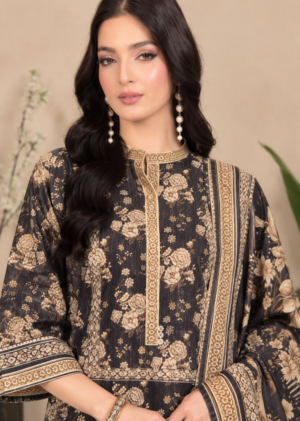A woman modeling a black and beige printed traditional kurta with ornate gold-toned border details, shown against a soft beige studio background.
