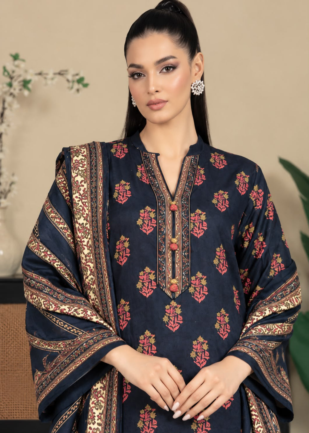 A woman modeling a dark navy blue kurta with red and gold floral prints and wide patterned borders, paired with a matching dupatta, set against a warm beige background.