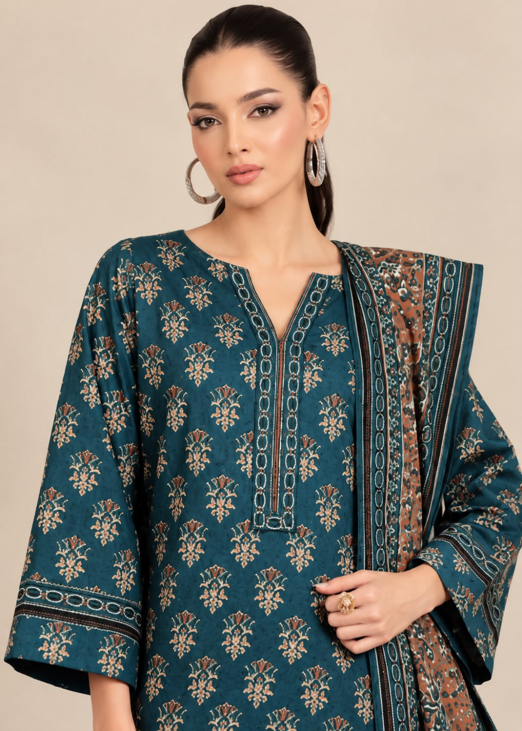 A woman modeling a teal blue printed kurta with beige and brown floral motifs, paired with a matching patterned dupatta, against a solid beige background.
