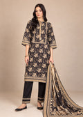 A woman models a traditional three-piece salwar kameez suit in black with beige floral prints and borders, paired with black trousers and a matching printed dupatta, set against a solid beige studio background.