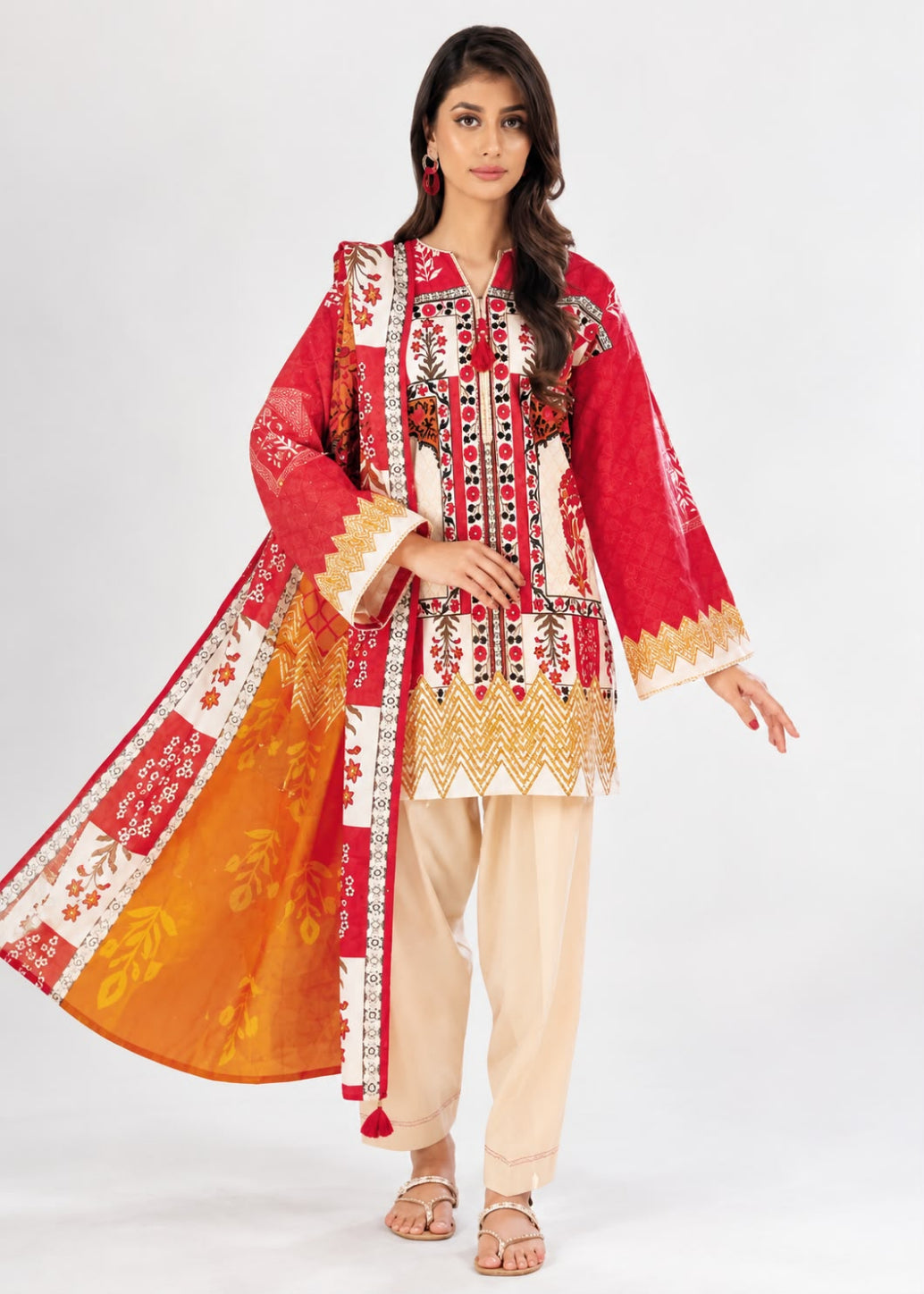 A woman modeling a traditional South Asian outfit featuring a red kurta with intricate gold and white embroidery, beige pants, and a bright orange dupatta with red and white patterns, set against a plain white studio background.
