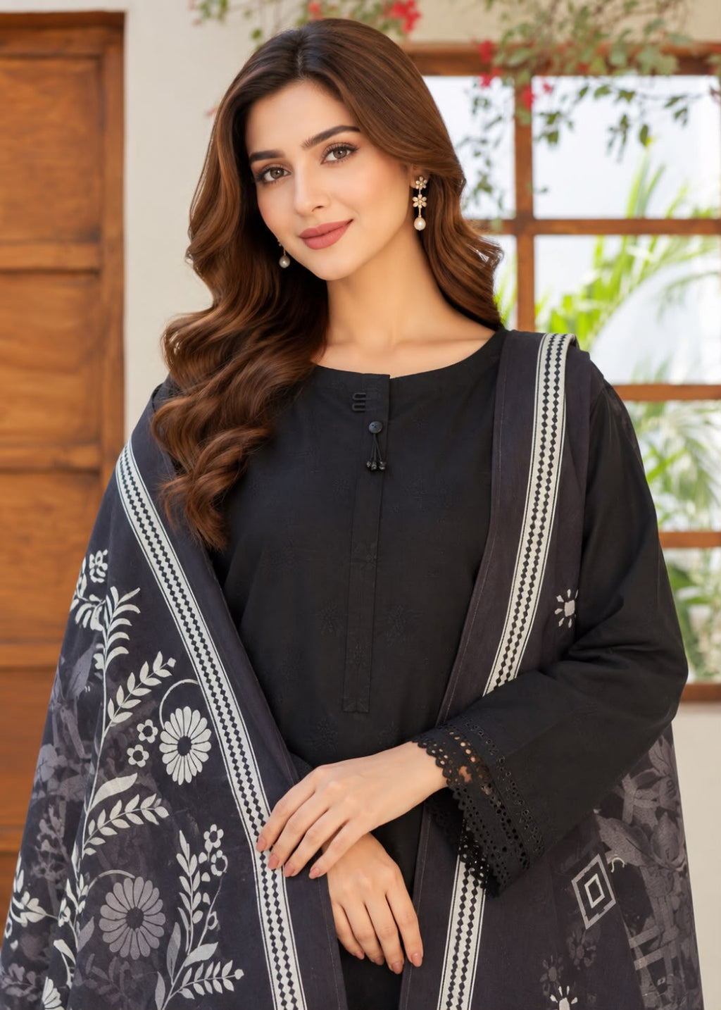 A woman modeling a black three-piece salwar kameez suit with a matching printed dupatta. The suit features a black long-sleeve kurta with a buttoned neckline, paired with a black dupatta decorated with white floral patterns and silver borders.