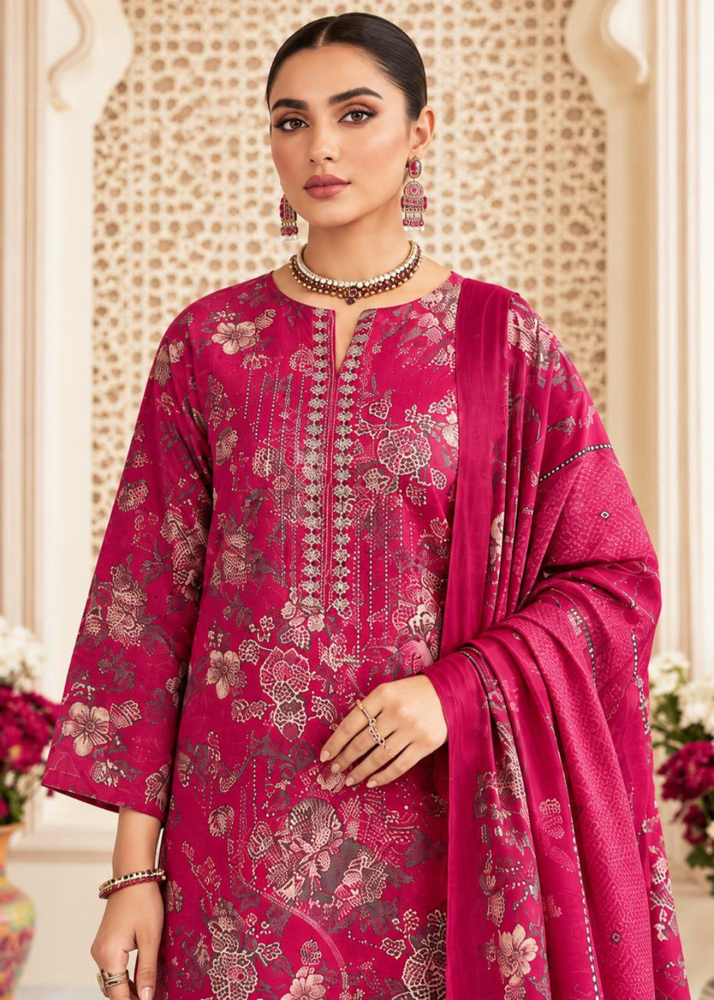 A woman models a traditional Indian salwar kameez suit in a rich magenta pink color, featuring intricate gold and silver floral embroidery, a matching embroidered kameez shirt, and a coordinating dupatta, set against an ornate beige background.