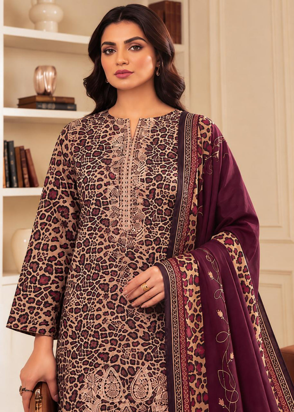 A woman modeling a three-piece Indian ethnic suit. The set features a beige and brown leopard-print kurta with intricate embroidery, a matching dupatta with paisley and floral patterns, and a deep purple border.