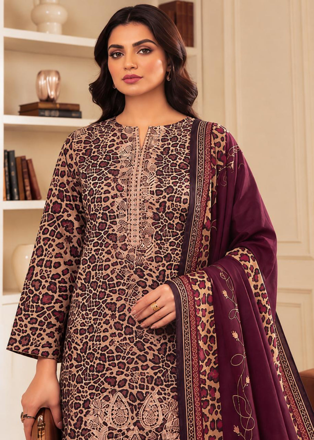 A woman modeling a three-piece Indian ethnic suit. The set features a beige and brown leopard-print kurta with intricate embroidery, a matching dupatta with paisley and floral patterns, and a deep purple border.