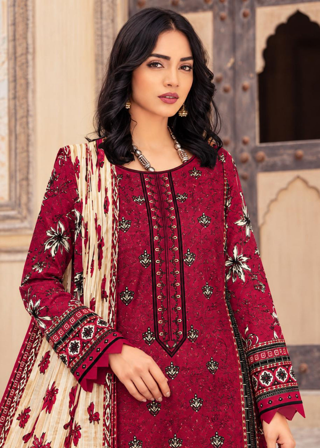 A woman modeling a traditional three-piece salwar kameez suit. The kurta is deep red with black and gold printed patterns and a central vertical gold embroidered placket.