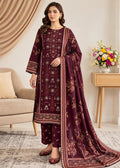 A woman models a traditional South Asian salwar kameez suit in deep maroon with intricate gold and beige floral embroidery, paired with a matching dupatta, in a styled indoor room setting.