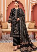 A woman models a black three-piece ethnic suit with intricate gold embroidery, featuring a long kurta, matching trousers, and a draped dupatta, set against a warm, arched architectural background.