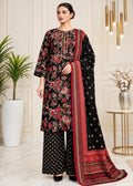 A woman models a traditional black three-piece salwar kameez suit with intricate red and gold floral embroidery, matching wide-leg trousers, and a coordinating dupatta, set against an elegant indoor background.