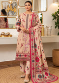 A woman models a traditional three-piece salwar kameez suit in a warm beige/peach color, decorated with vibrant pink, red, and blue floral prints. The set includes a long-sleeved tunic, matching trousers, and a coordinating dupatta draped over her shoulder, set against an elegant indoor background with mirrors and gold-framed wall art.
