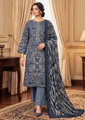 A woman models a traditional Indian salwar kameez suit set in a luxurious room. The set features a navy blue kurta with intricate white floral embroidery, matching navy blue trousers, and a coordinating navy blue dupatta with a bold zari pattern.