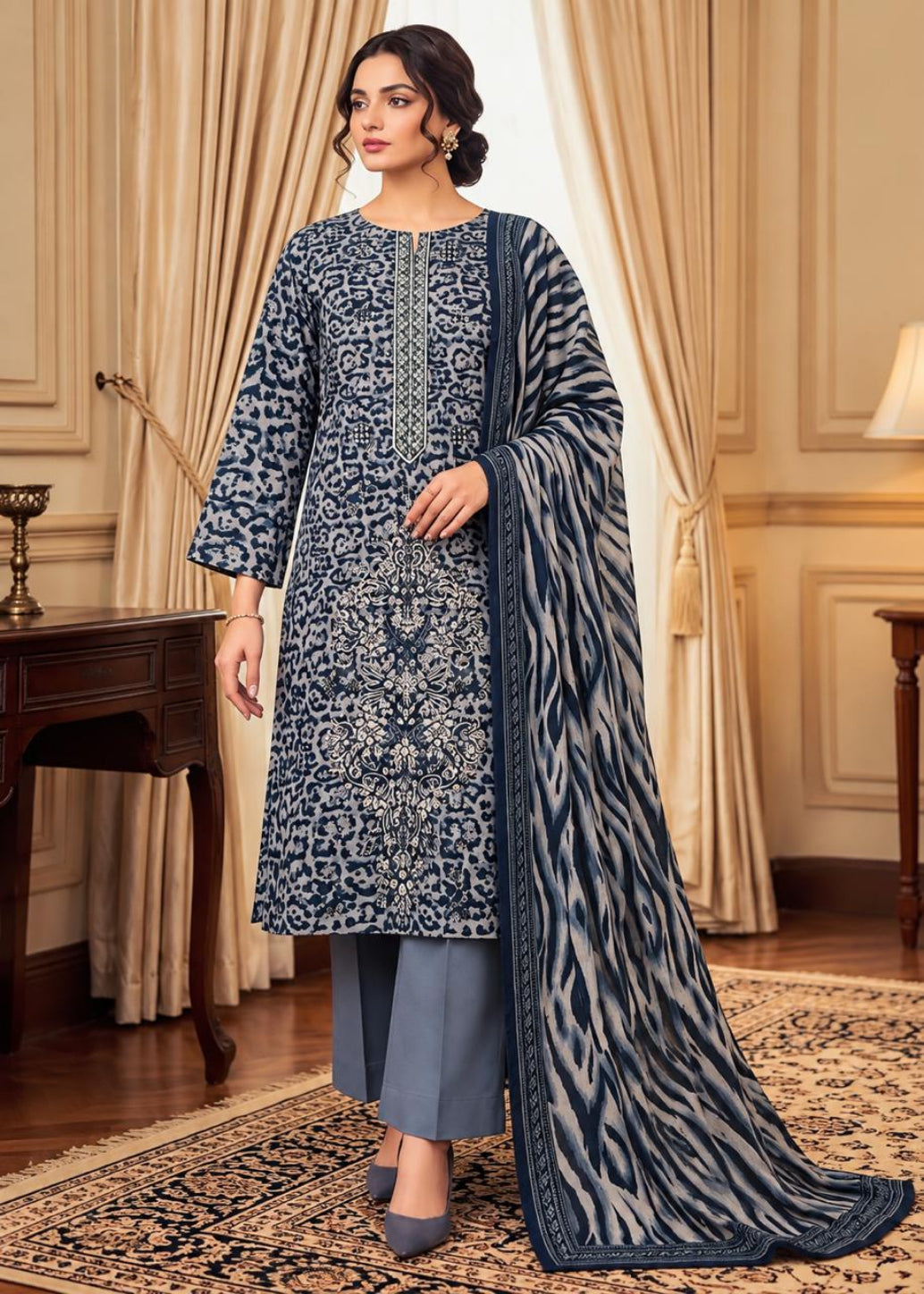 A woman models a traditional Indian salwar kameez suit set in a luxurious room. The set features a navy blue kurta with intricate white floral embroidery, matching navy blue trousers, and a coordinating navy blue dupatta with a bold zari pattern.