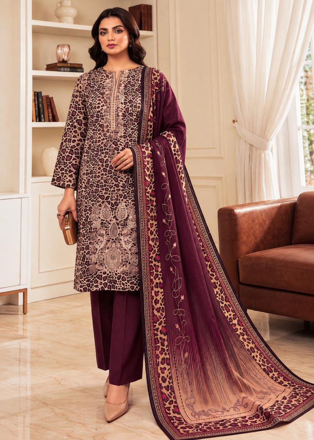 A woman models a traditional Indian salwar kameez suit set in a bright, elegant room. The set features a deep maroon kurta and trousers with a beige and brown leopard print kameez overlay, and a matching maroon dupatta with a beige-to-brown gradient and floral border.