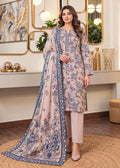 A woman models a traditional three-piece salwar kameez suit set in a beautifully decorated room. The set features a light beige kurta with blue floral prints, matching beige trousers, and a coordinating dupatta with a blue border and floral print.