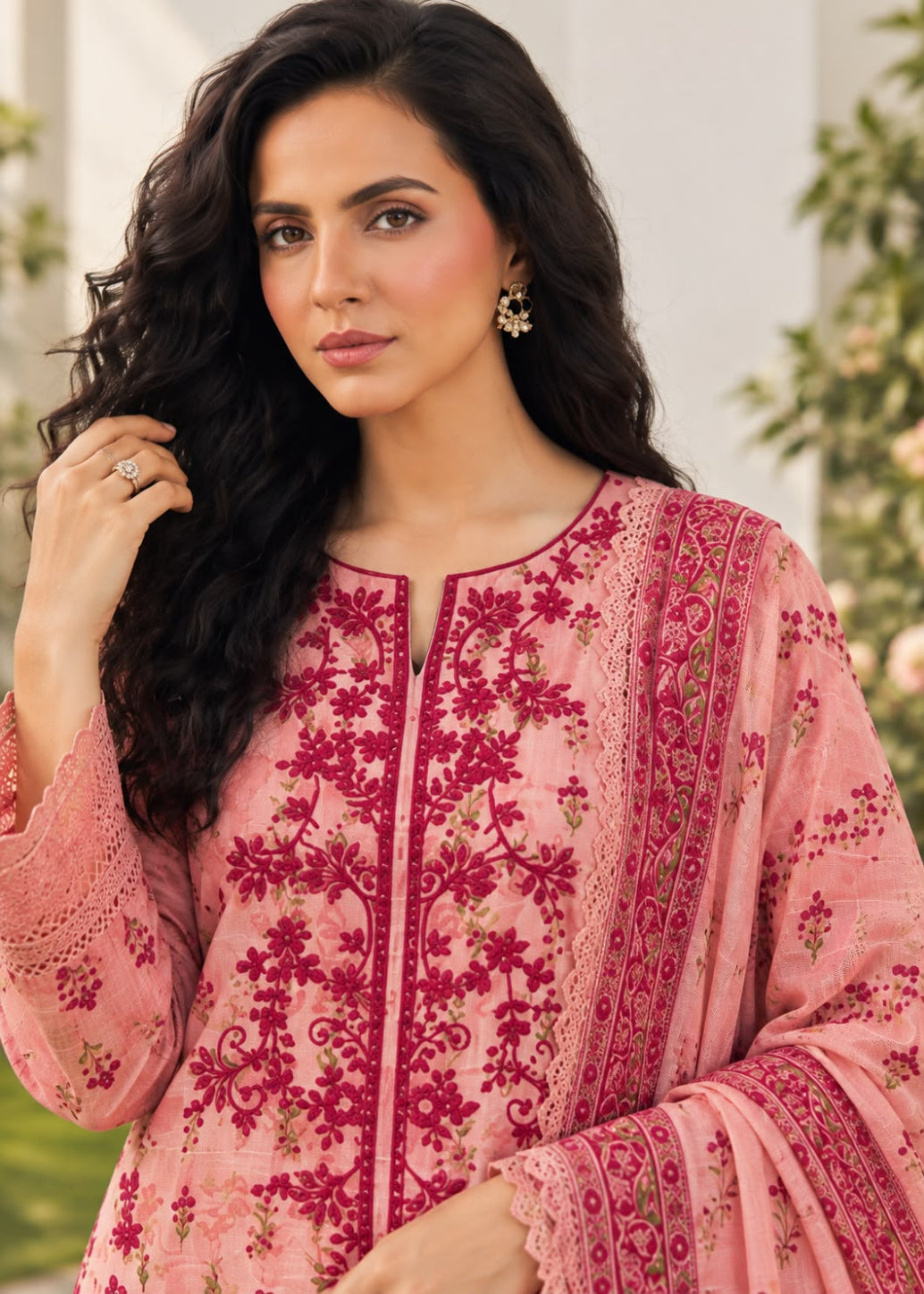 A woman wearing a pink embroidered traditional outfit with a matching sheer dupatta, featuring intricate magenta floral embroidery and lace details.