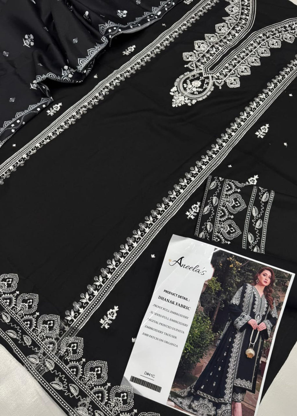 Black ethnic fabric with intricate silver embroidery and border detailing, shown with a printed fabric card featuring a model wearing the finished garment.