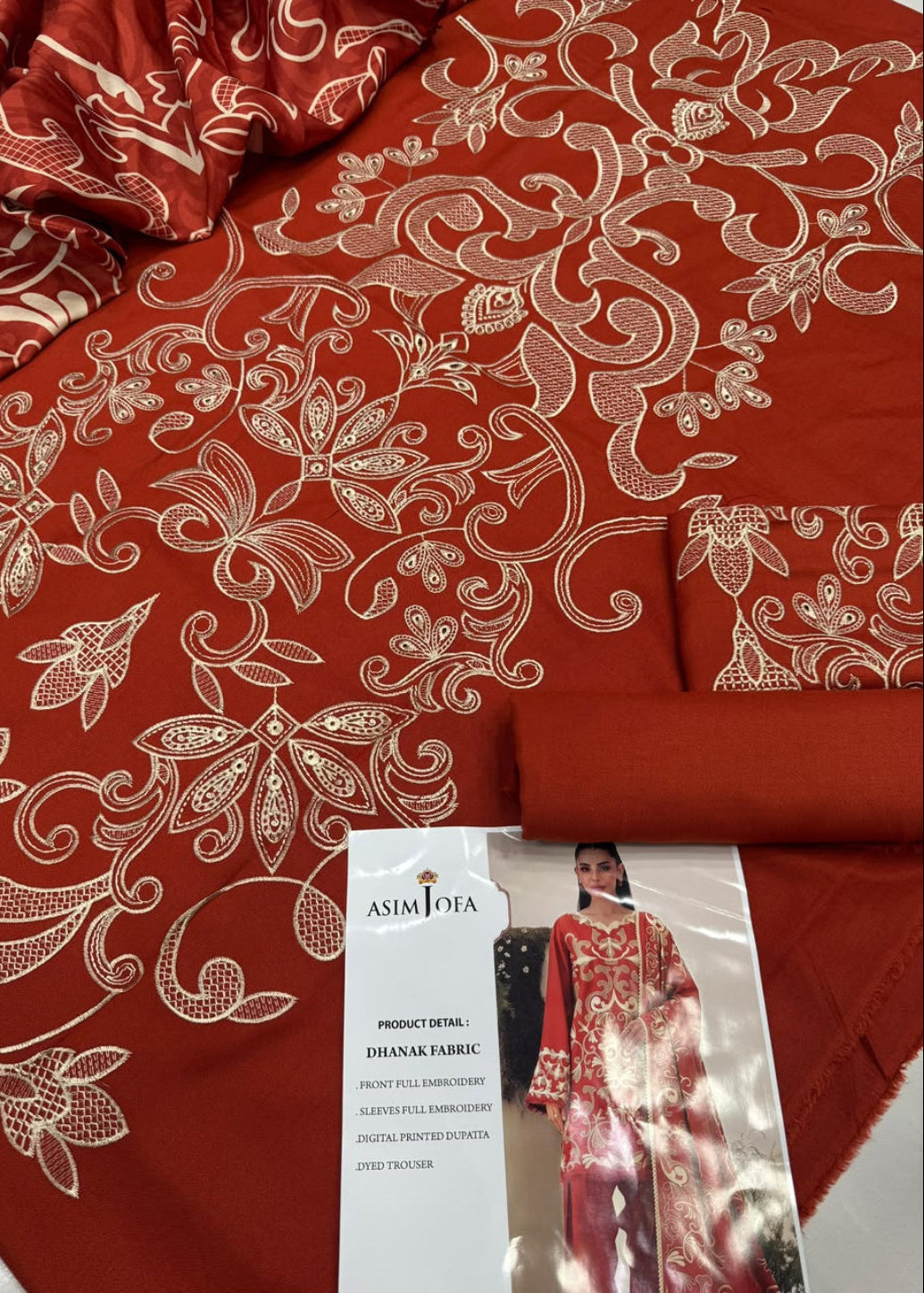 A folded piece of rust-red or terracotta-colored fabric with intricate cream floral and vine embroidery, shown alongside a printed product tag reading 'ASIM LOYA' and 'DIHNAK FABRIC'.