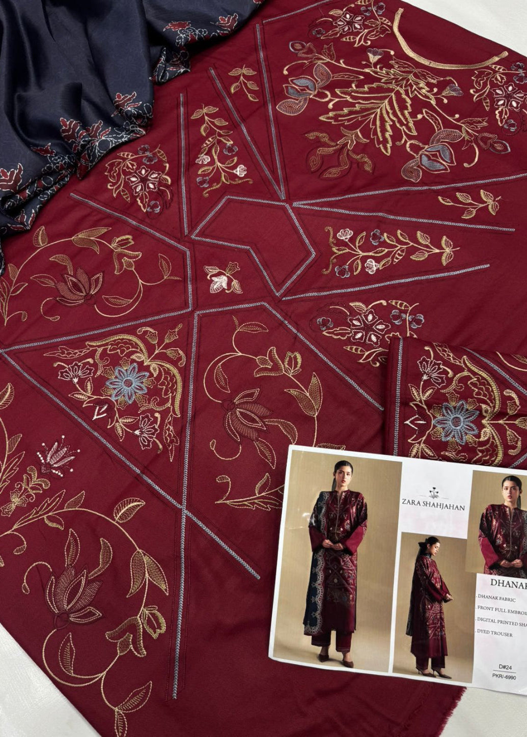 A deep maroon embroidered kurta set with geometric borders, gold floral embroidery, and blue accents, shown alongside a navy blue fabric piece and a printed catalog card featuring model photos.