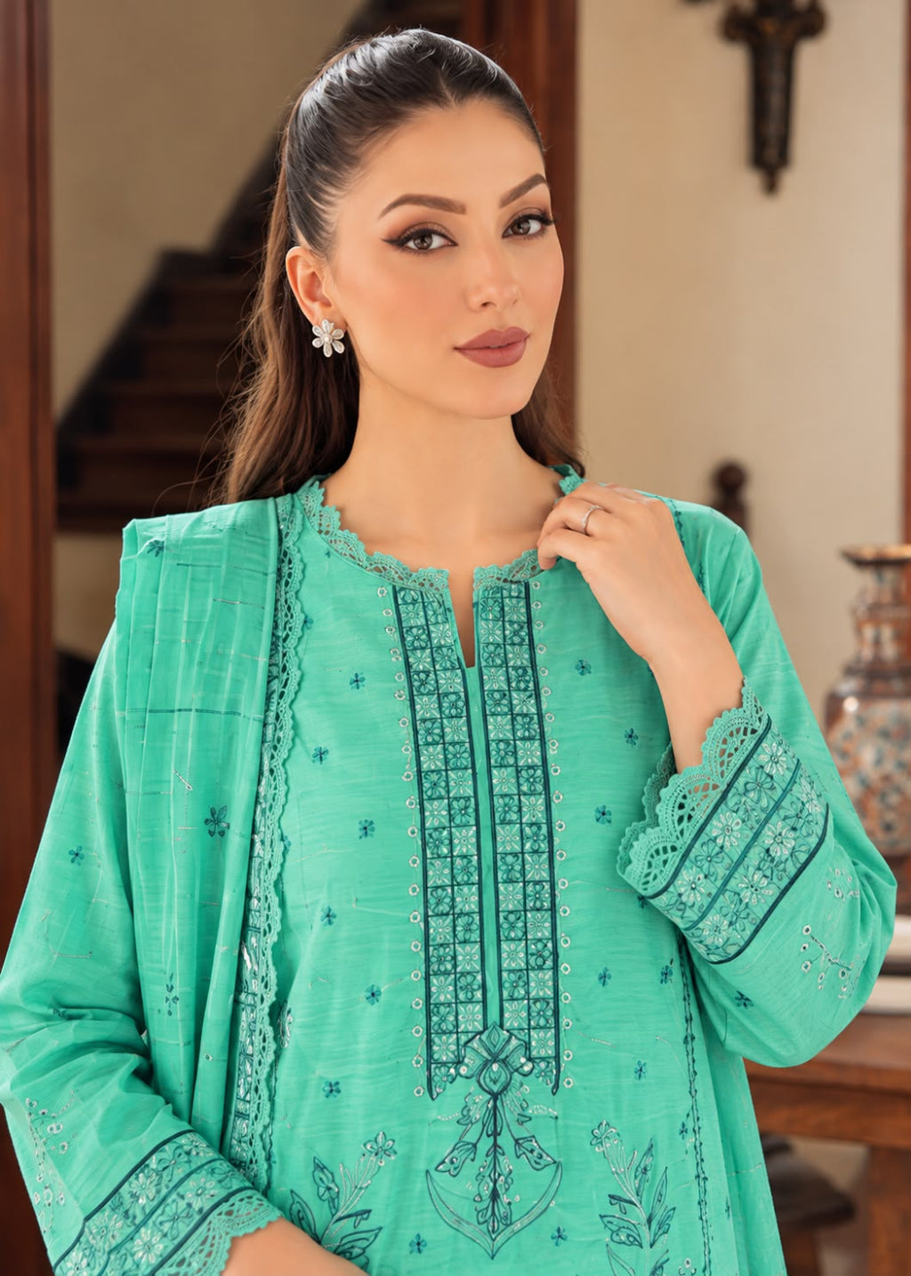 A woman wearing a mint green embroidered traditional tunic with matching embroidered sleeves, posed in an indoor setting with a staircase in the background.