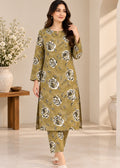 A woman models a three-piece olive green kurta set with a large white and gray floral print, featuring a long-sleeve tunic, matching pants, and a coordinating belt, set against a warm beige interior background.