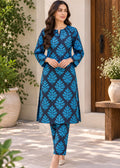 A woman modeling a blue and teal printed kurta set with matching pants, standing in a garden courtyard setting.
