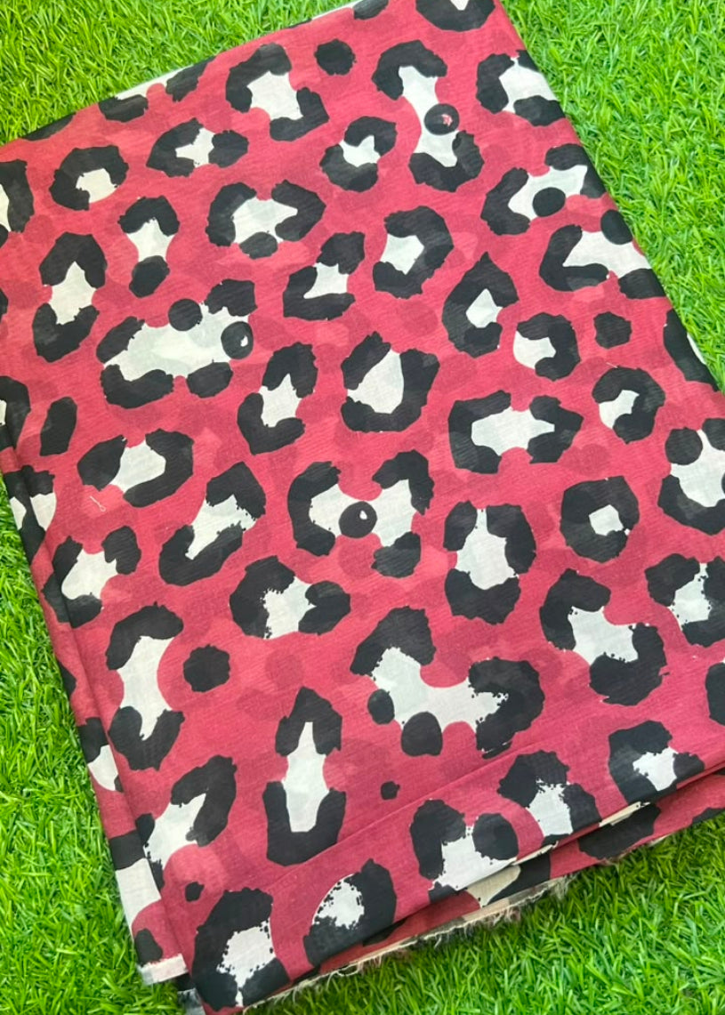 A folded piece of fabric with a pink, black, and white leopard print pattern, laid flat on a green grass background.