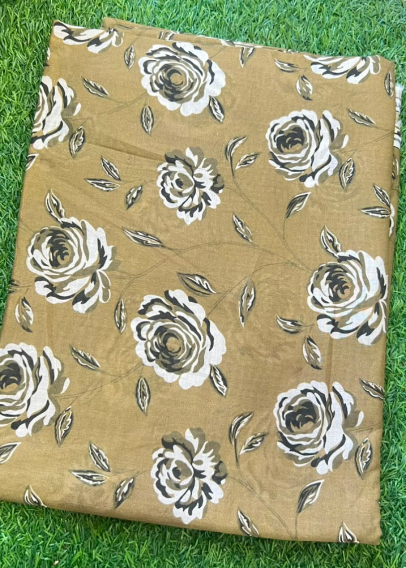 A folded piece of tan fabric with a white and gray rose floral print, laid flat on green grass.