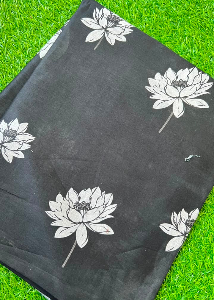 A folded black fabric item, likely a scarf or sari, featuring a white lotus flower pattern, laid flat on a green grass background.