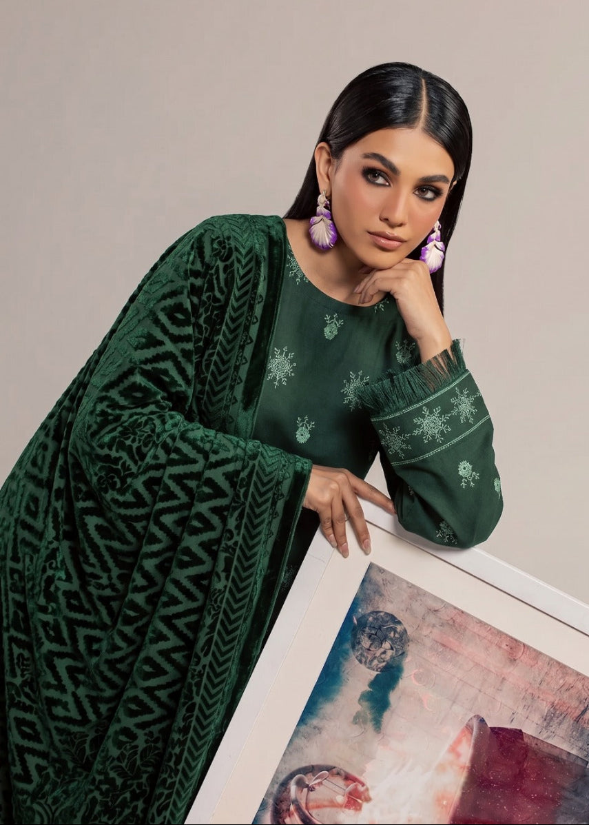 A woman models a dark green traditional outfit with a matching embroidered cardigan and large purple earrings, holding a framed abstract art print against a neutral beige background.