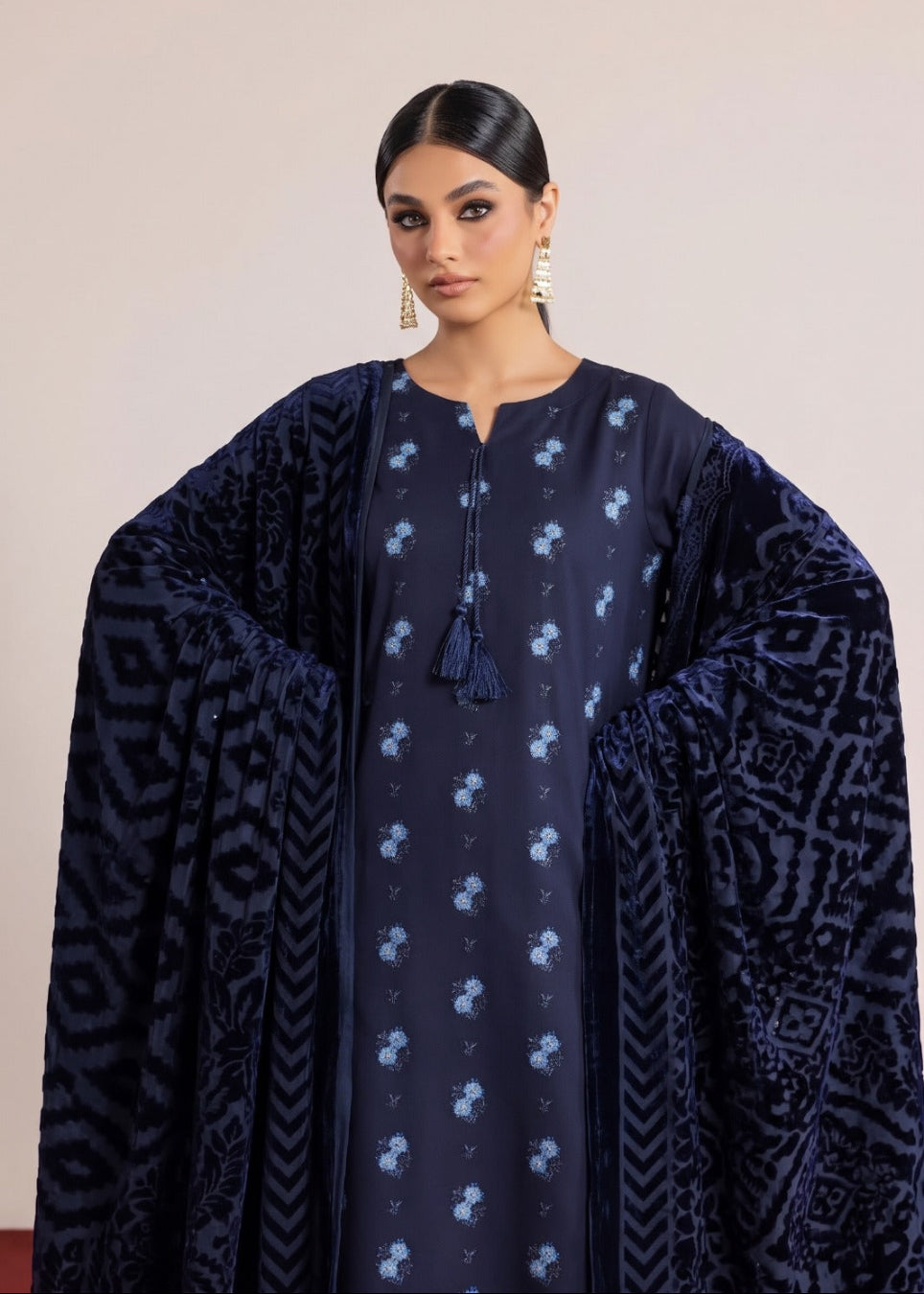 A woman modeling a navy blue traditional outfit with a matching patterned shawl, set against a solid beige studio background.