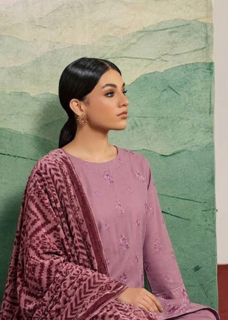 A woman models a traditional three-piece salwar kameez suit in dusty purple with a matching patterned dupatta, posed against a green watercolor mountain backdrop.