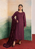 A woman models a deep plum purple traditional Indian salwar kameez suit with matching embroidered kurta, trousers, and a long dupatta, set against a scenic painted backdrop.