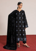 A woman models a black traditional outfit with light blue printed motifs and a matching black dupatta, standing on a red carpet against a beige studio backdrop.