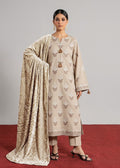 A woman models a traditional beige Anarkali kurta set with matching trousers and a patterned dupatta, standing on a red carpet against a neutral gray background.