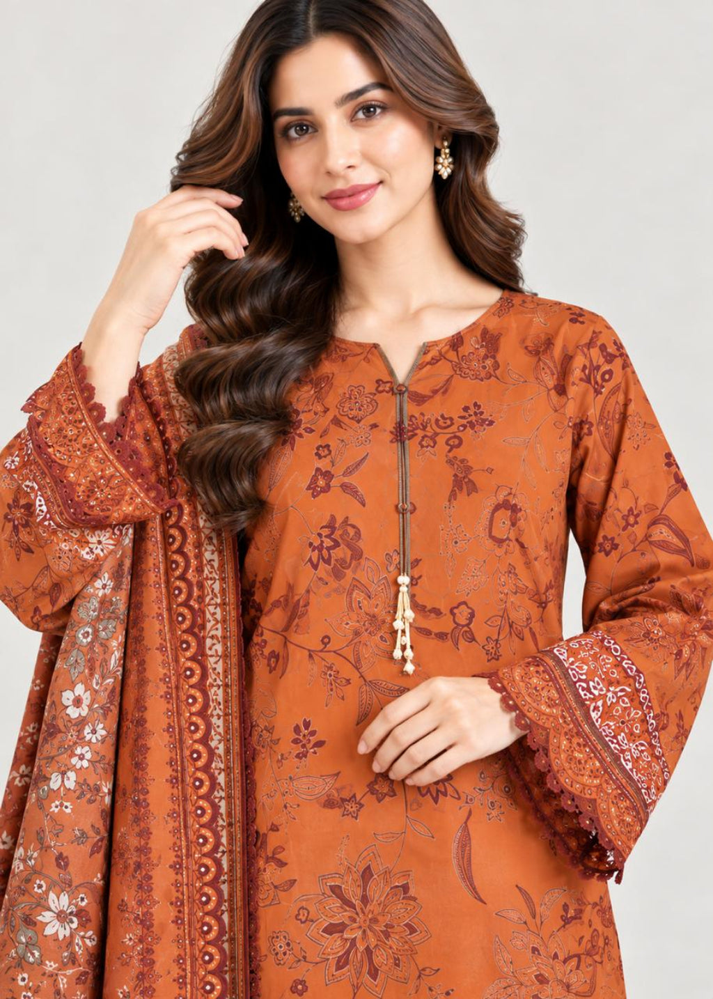 A woman modeling a rust-orange printed kurta with matching printed dupatta, featuring a split neckline, tassel zipper, and wide sleeves with lace cuffs, set against a plain light gray background.