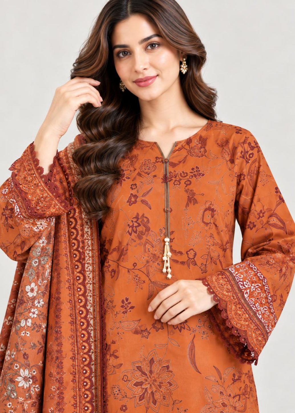A woman modeling a rust-orange printed kurta with matching printed dupatta, featuring a split neckline, tassel zipper, and wide sleeves with lace cuffs, set against a plain light gray background.