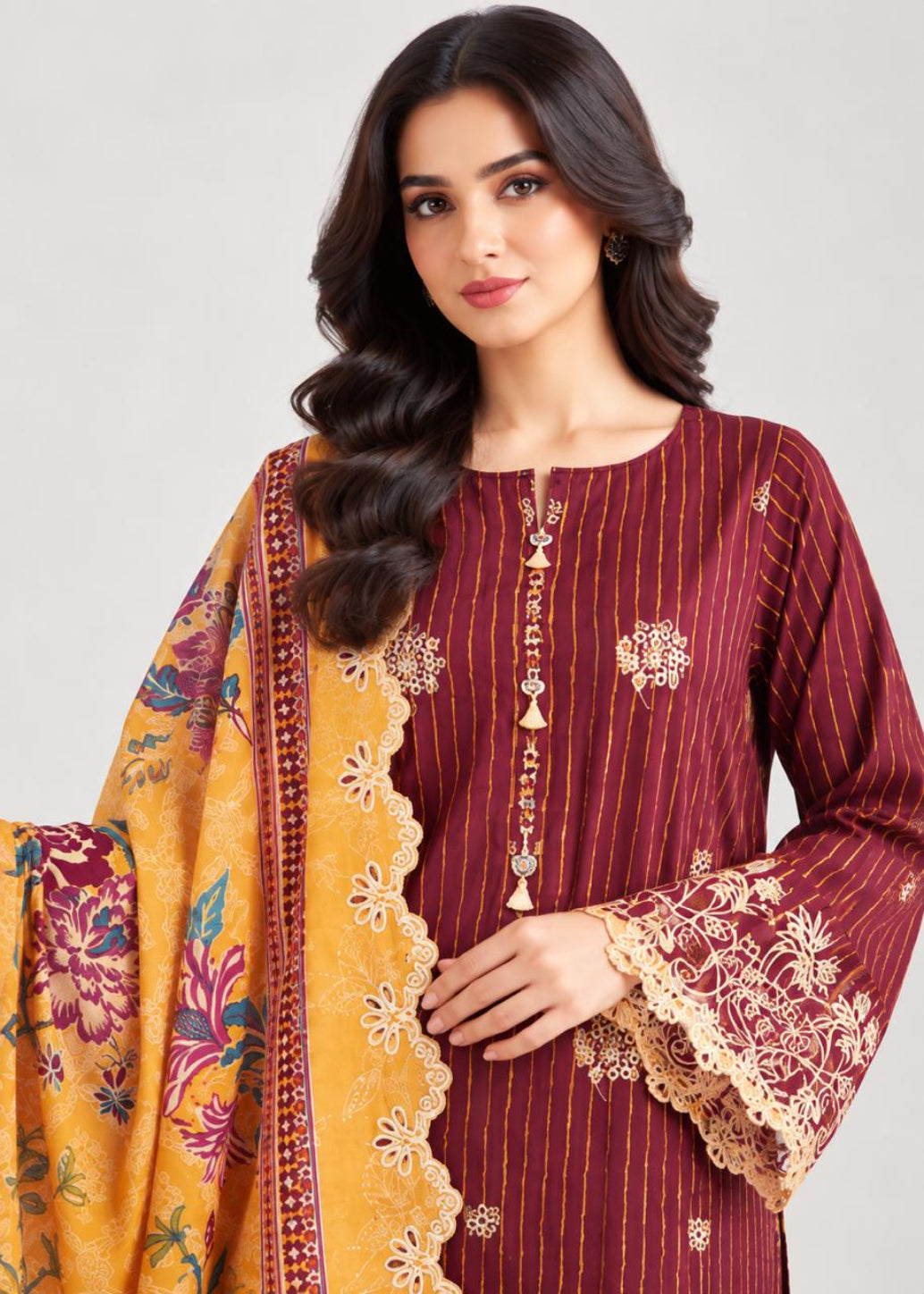 A woman modeling a traditional South Asian salwar kameez set. The kurta is deep maroon with thin vertical gold stripes and gold floral embroidery on the front placket and bell sleeves, paired with a mustard yellow dupatta featuring a floral print and scalloped border.
