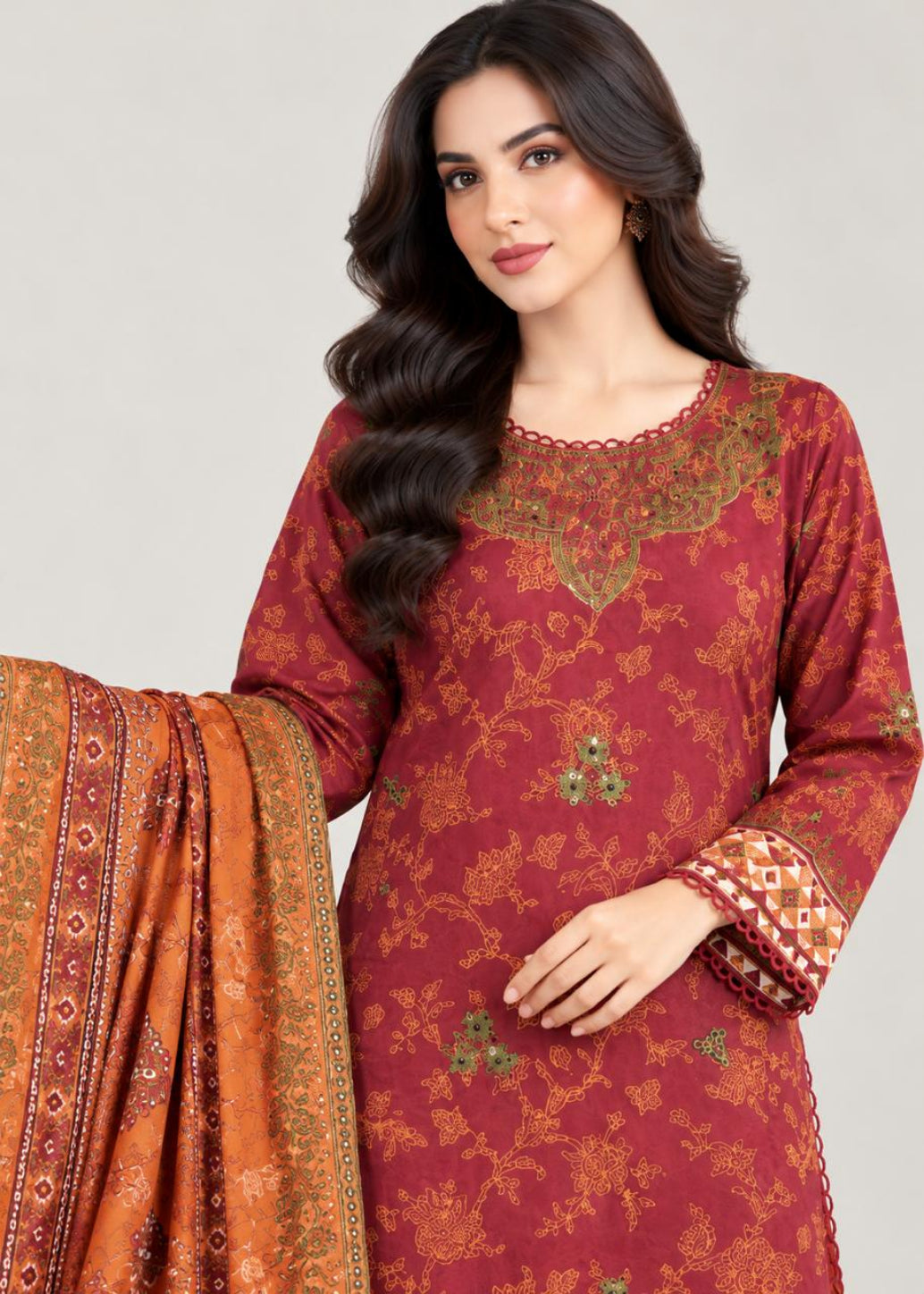 A woman modeling a traditional Indian salwar kameez suit. The kurta is a deep maroon red with intricate gold and green floral patterns, featuring a gold embroidered yoke and patterned cuffs.
