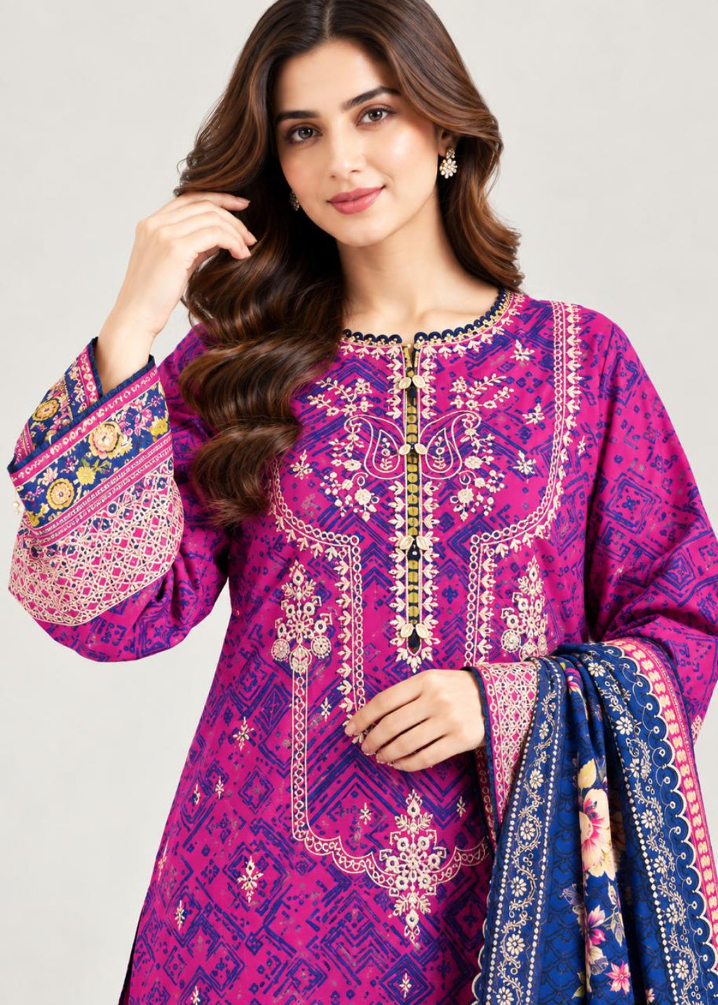 A woman modeling a bright magenta and purple printed kurta with intricate gold, white, and blue embroidery, paired with a navy blue dupatta featuring floral patterns, set against a plain light gray background.